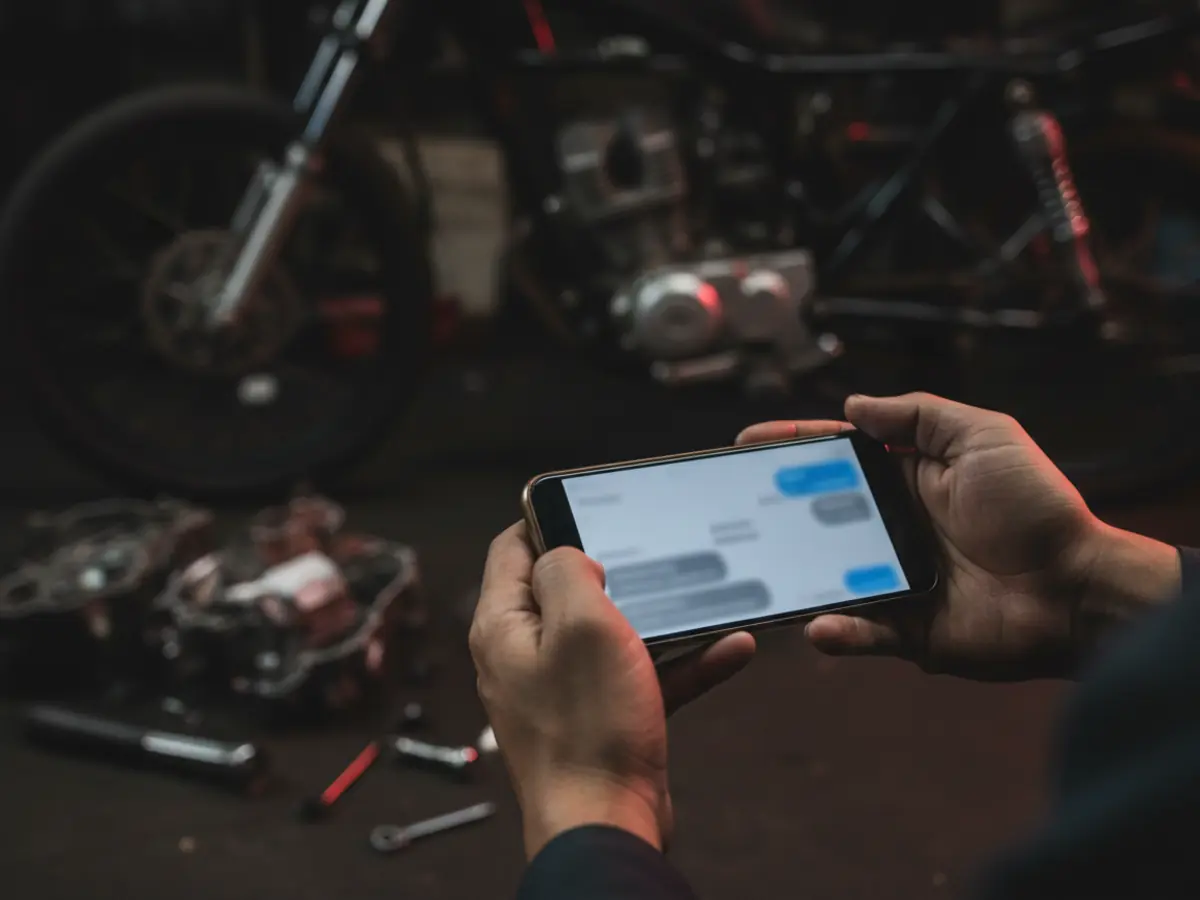 Mekanik memegang ponsel untuk chat WhatsApp dengan tim grosir